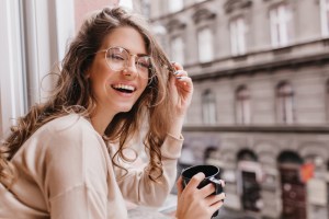 woman sitting by a window and smiling while holding a cup of coffee